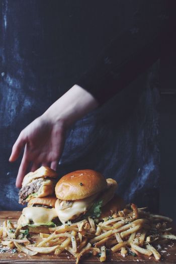 Cropped hand of woman holding burgers over french fries in darkroom