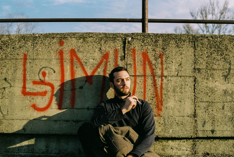 Young man smoking cigarette against retaining wall