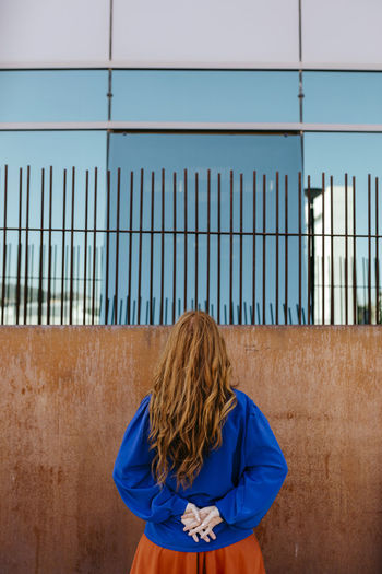 Rear view of woman standing with hands behind back while facing wall
