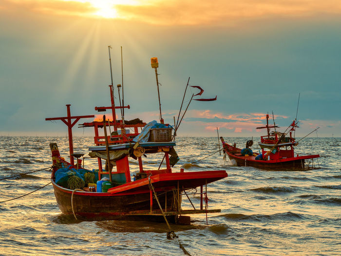 Fishing boats moored on sea against sky during sunset
