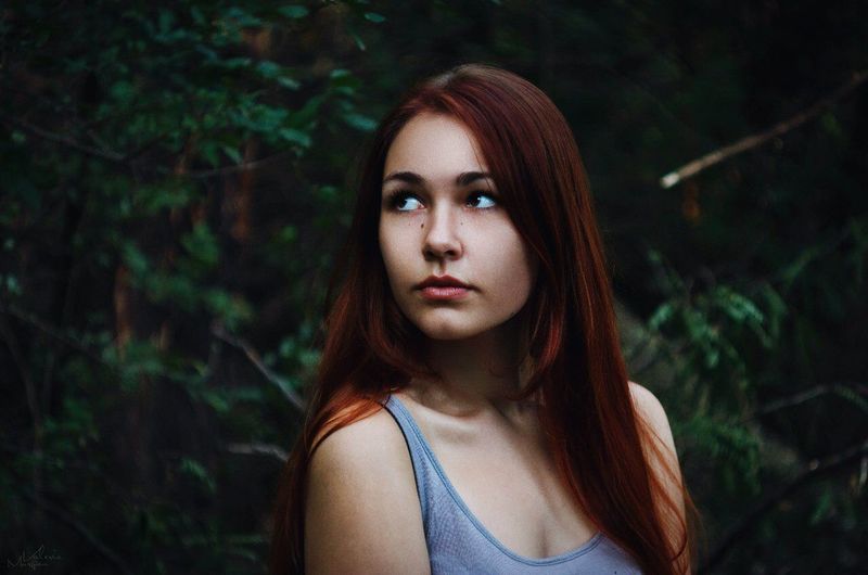 Thoughtful young woman standing by trees in forest
