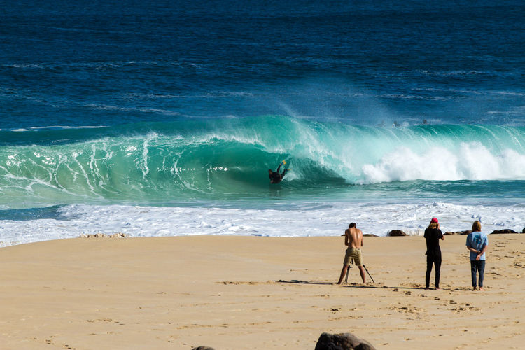 Rear view of people watching at surfer in sea