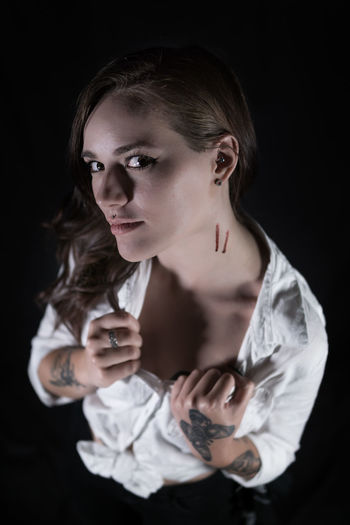 Portrait of young woman showing wounds on neck against black background