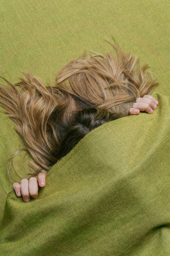 From above of anonymous female with long fair hair covering face with green fabric