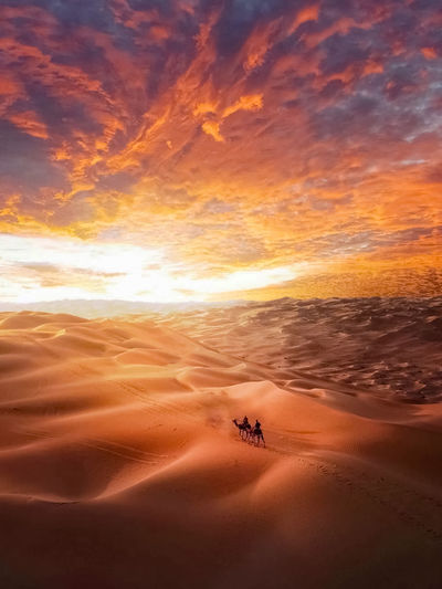 Scenic view of desert against dramatic sky during sunset