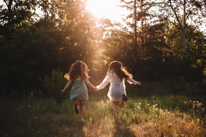 Back view of girlfriends holding hands while running in summer forest
