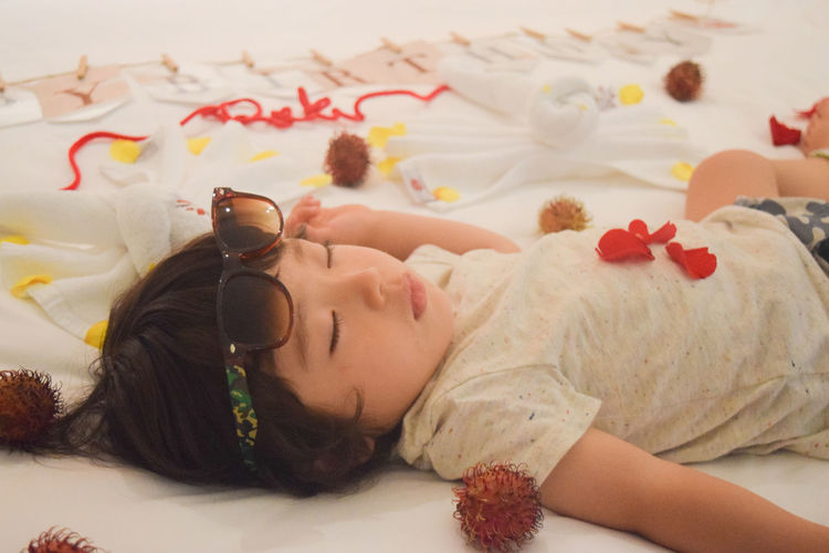 High angle view of cute girl sleeping by petals and rambutans on bed