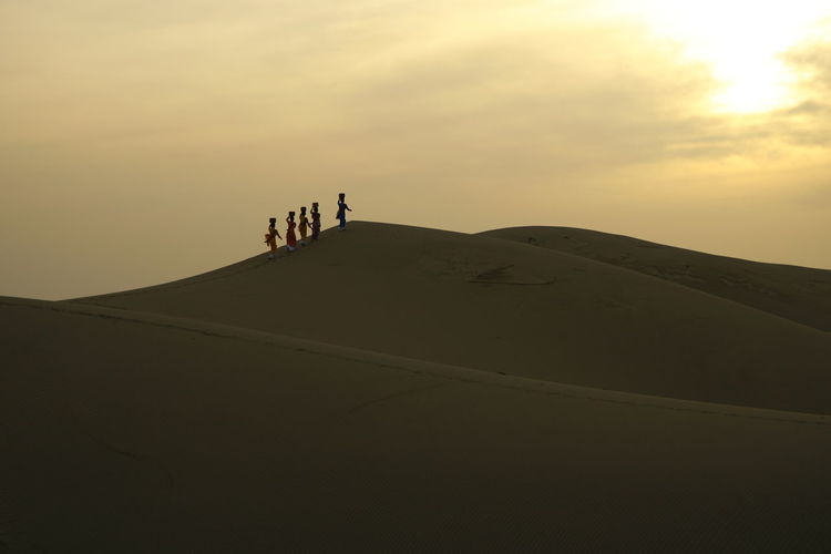 People riding in desert against sky during sunset