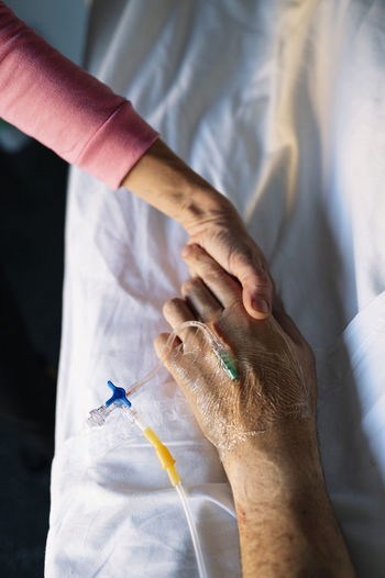 Woman holding patient hand on bed in hospital