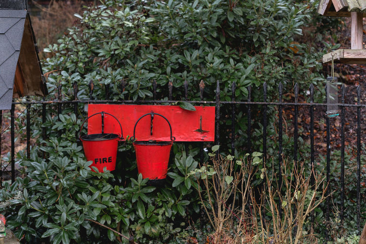 Red fire buckets hanging on railing by plants