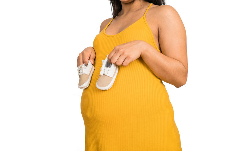 Midsection of woman holding yellow while standing against white background