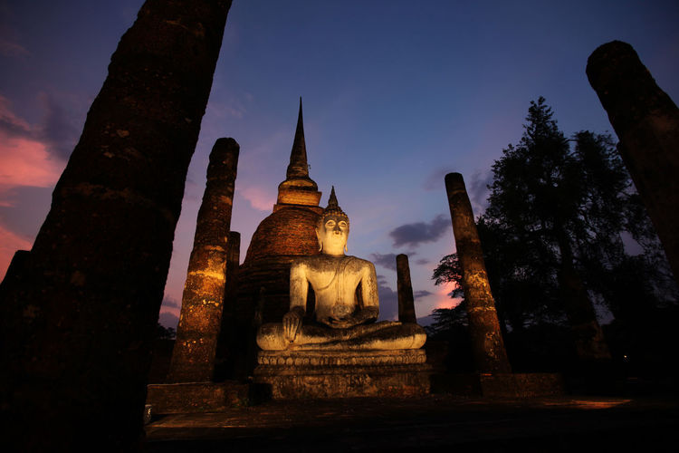 Low angle view of buddha statue and temple against sky at night