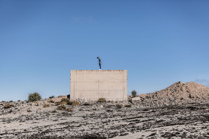 Man standing on retaining wall against clear blue sky at desert