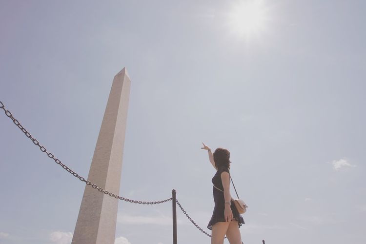 Low angle view of mid adult woman pointing at washington monument during sunny day