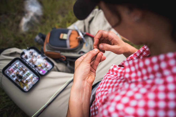 Woman angler ties fly onto end of fly fishing line while sitting