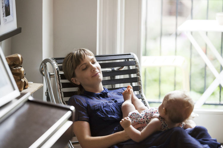 Happy mother sitting with baby girl on lounge chair at home