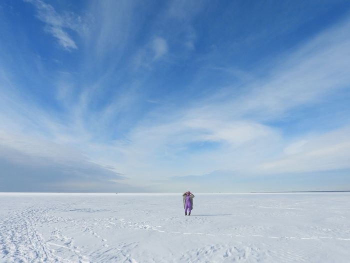 Rear view of woman walking on snow covered landscape against sky