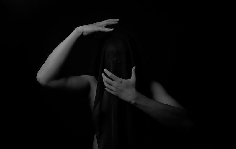 Portrait of woman covering face against black background