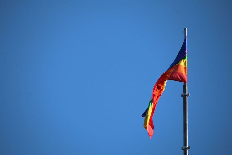 Rainbow flag waving against clear blue sky