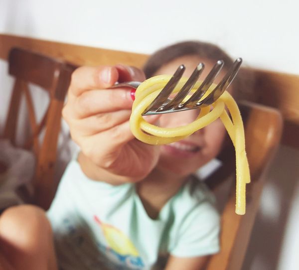 Close-up of girl holding spaghetti on fork at home