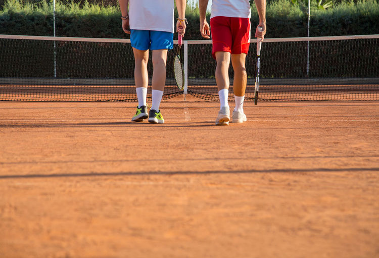 Low section of male friends playing tennis on court