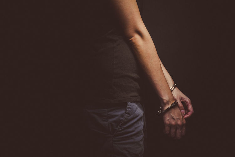 Midsection of man with handcuffs standing against black background