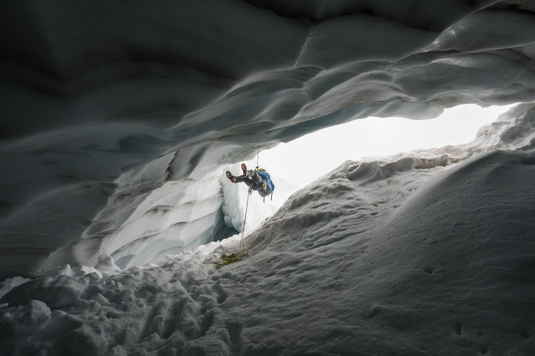 Mountain climber rappelling into crevasse / glacial ice cave.