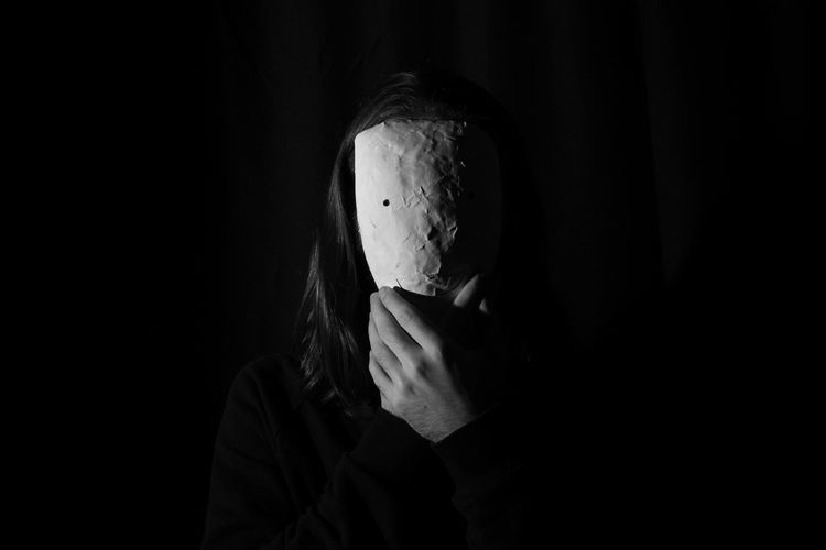 Portrait of man covering face against black background
