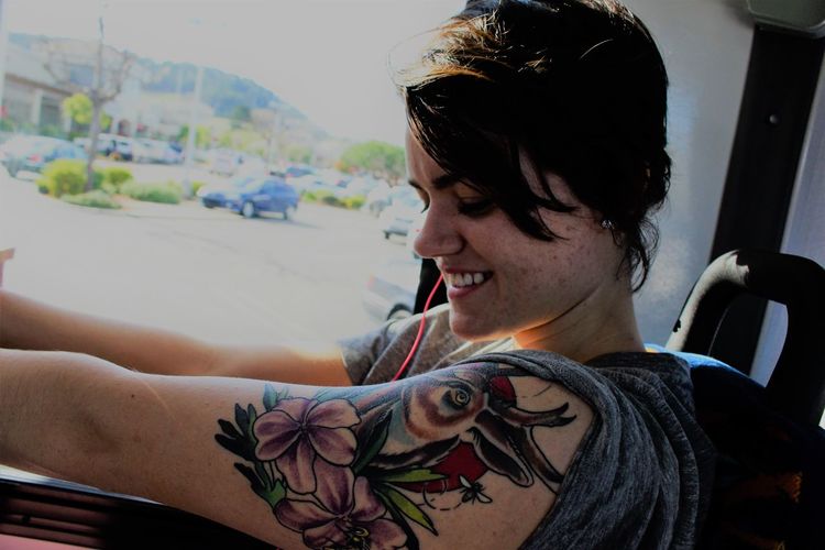 Smiling young woman with floral tattoo on arm traveling in bus
