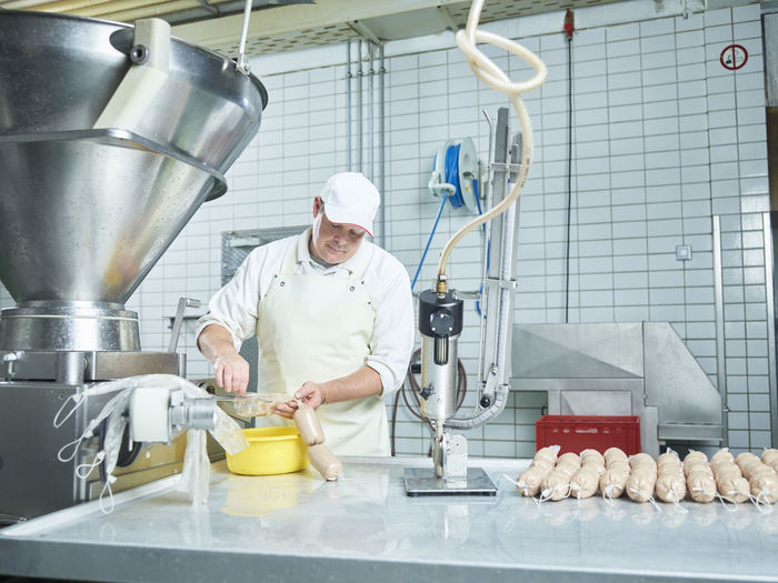 Butcher making fresh sausages through machinery in factory