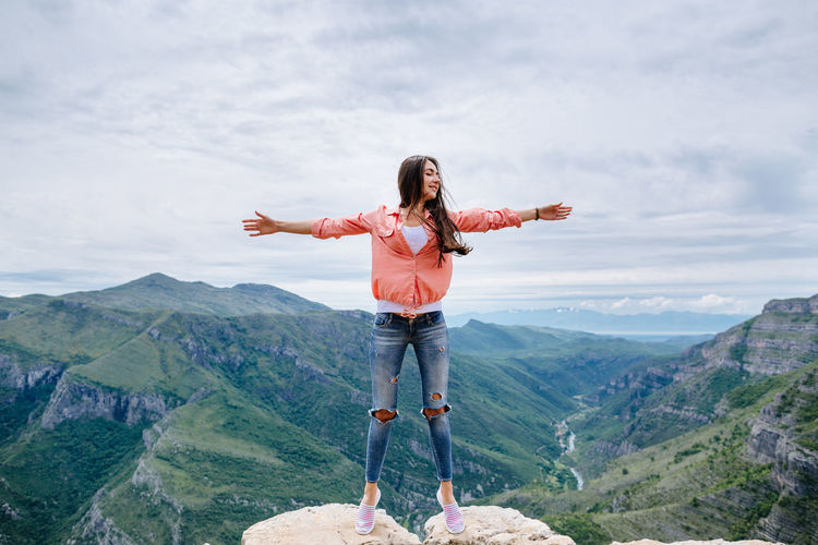 Beautiful woman with arms outstretched standing on cliff against mountain