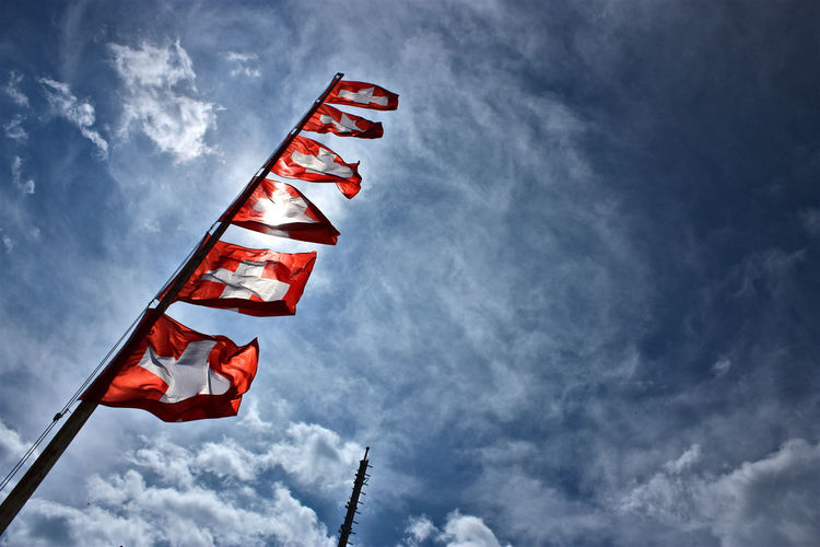 Low angle view of swiss flags on mast against sky