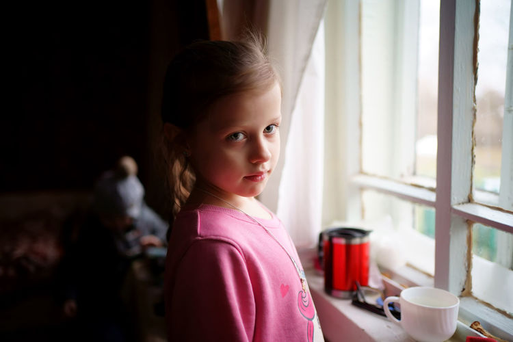 Portrait of cute girl standing against window