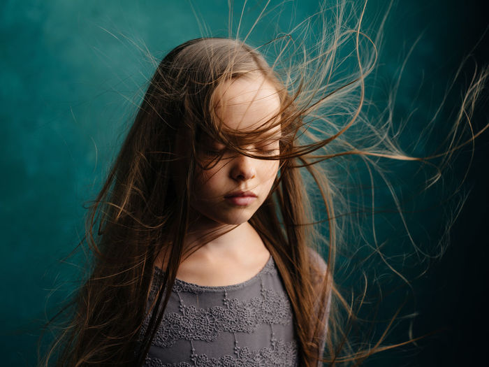 Girl with tousled hair standing against wall