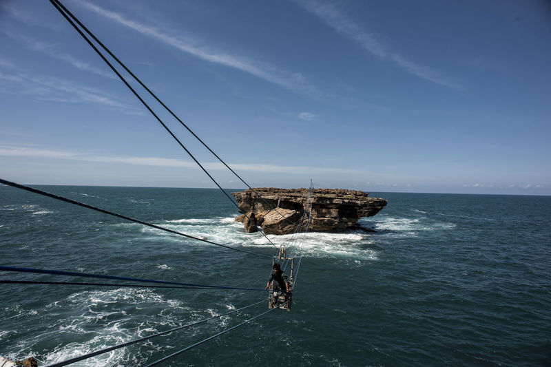 Man on overhead cable car over sea