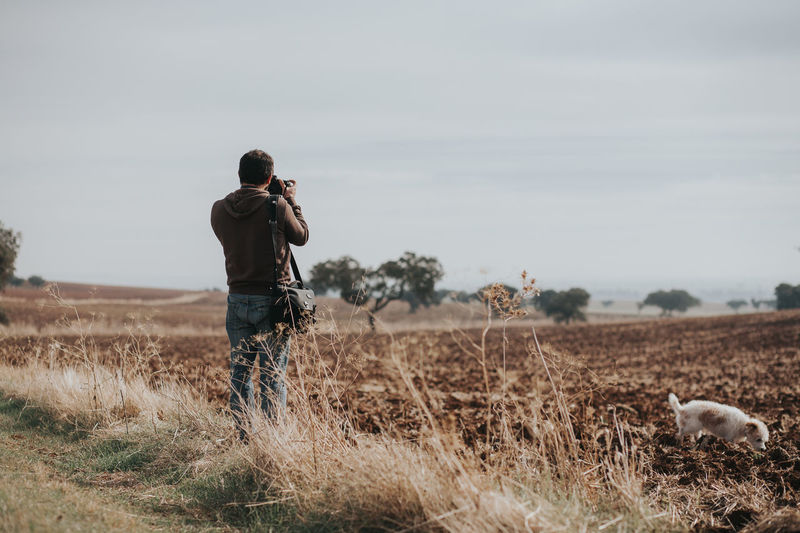 Rear view of man photographing while standing at farm against sky