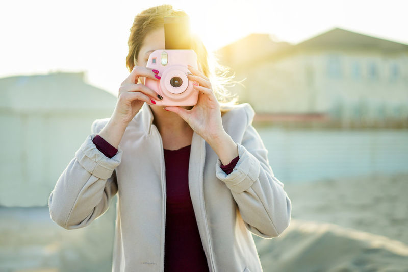 Woman holding instant camera while standing at beach