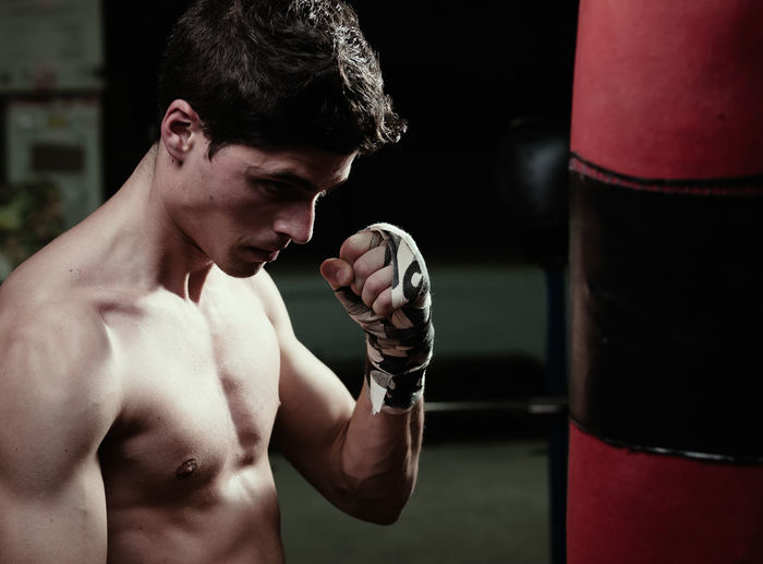 Shirtless man punching bag in boxing rink