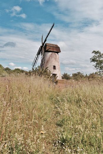 Low angle view of traditional windmill on grassy field against sky