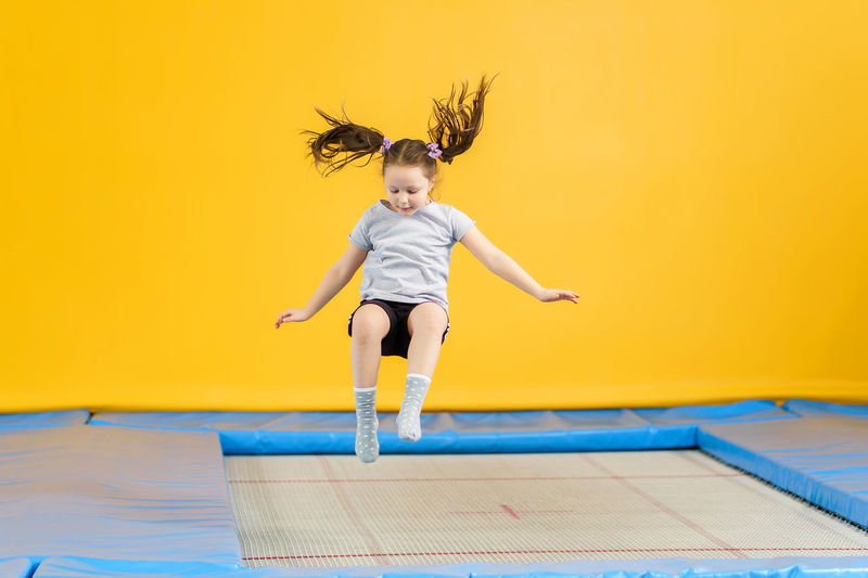 Full length of girl jumping against yellow wall