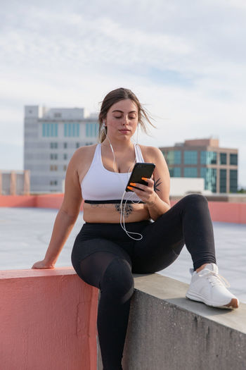 Curvy woman listens to music on mobile phone working out outdoors.