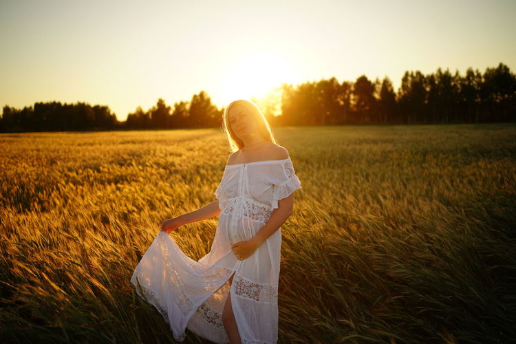 Happy pregnant woman stands in the field and touches belly nature. 