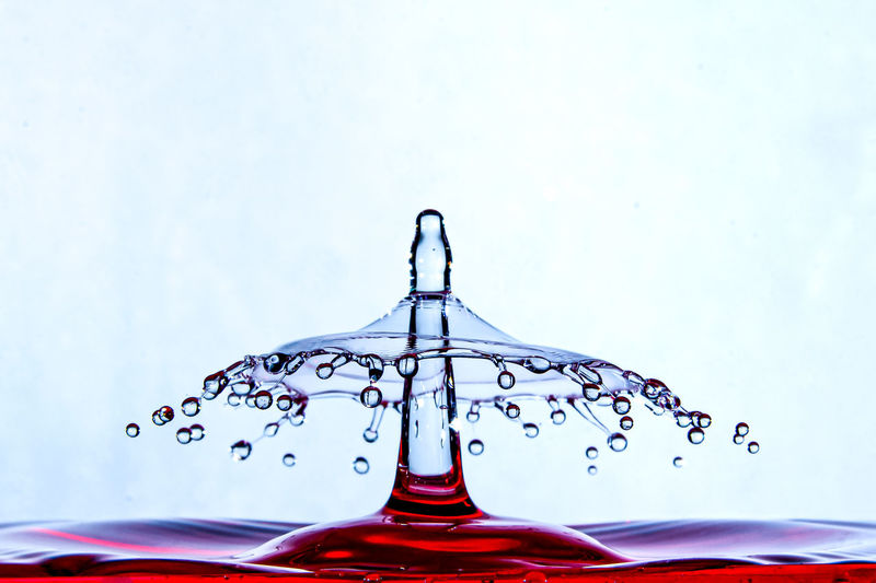 Close-up of drop splashing on water against white background