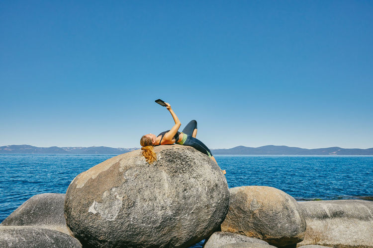 Bird on rock by sea against clear blue sky
