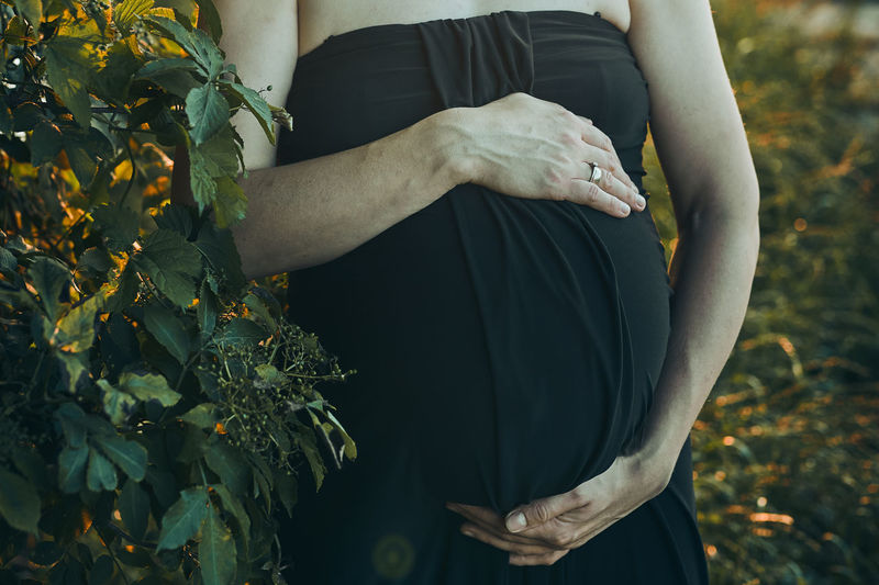 Pregnant woman hugging her tummy standing outdoors surrounded by nature. pregnancy, expectation
