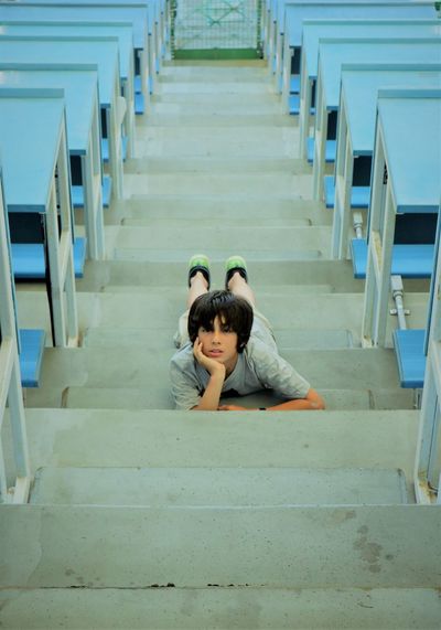 High angle portrait of boy lying on steps amidst benches