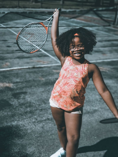 Smiling girl holding racket while standing on court during sunny day