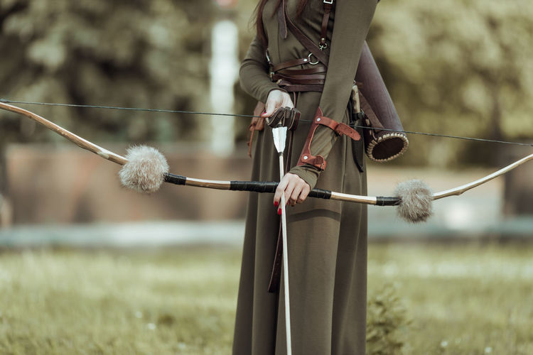 Midsection of woman holding longbow standing outdoors