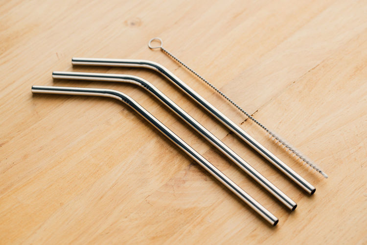 Top view of reusable metal straws and cleaning brush in row on wooden table