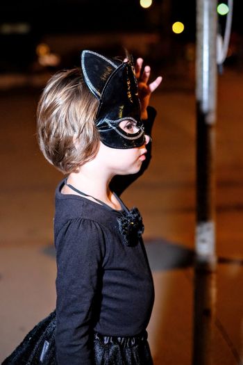 Profile view of girl wearing venetian mask in city at night during halloween